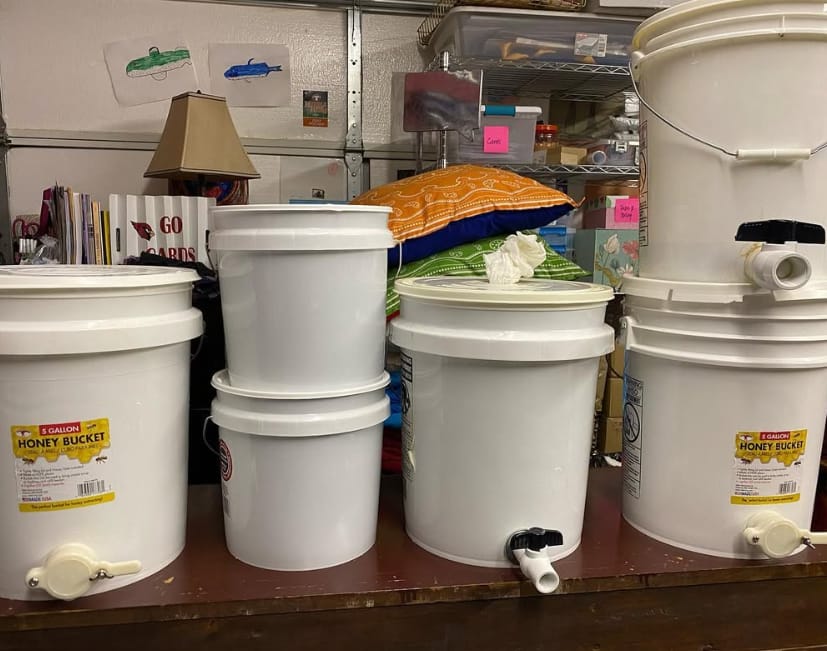 Five-gallon honey buckets with gates lined up in the workroom